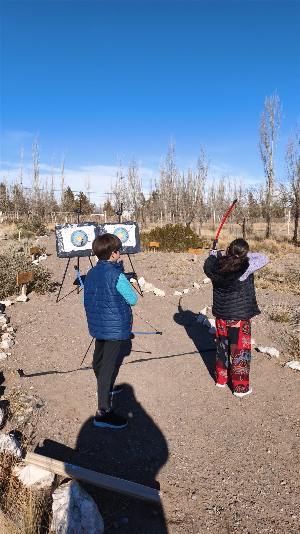 Dos personas practicando tiro con arco al aire libre en Malargüe con la cordillera de fondo